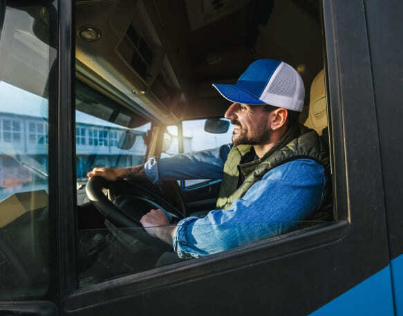 Truck driver wearing a hat smiles while driving his truck.