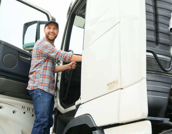 A carrier smiles standing at the open door of his truck cab.