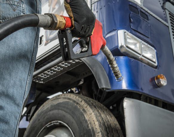 A truck driver wearing safety gloves and holding a fuel pump nozzle in their hand.