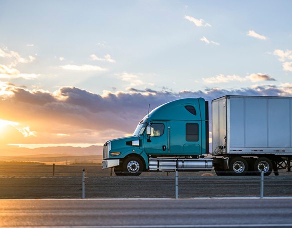 Semi truck driving on the road at sunset.