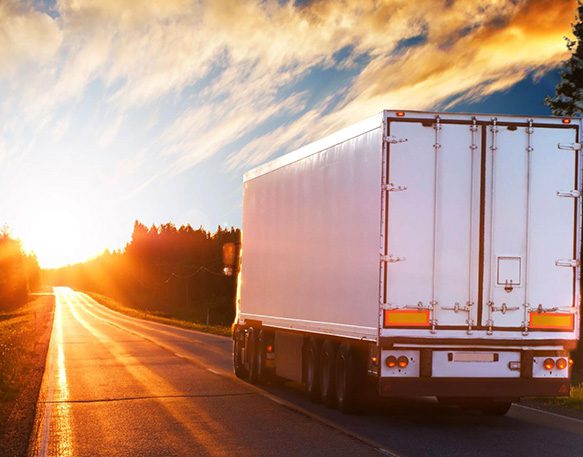 White semi truck driving on single lane asphalt rural road under clear skies at sunset.