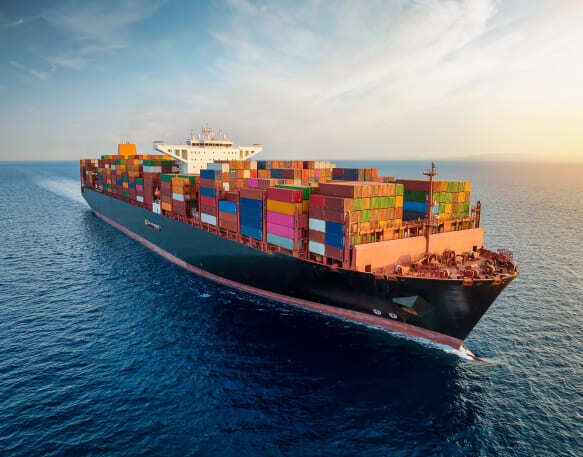 Aerial view of a large, loaded container cargo freight ship traveling over open ocean.