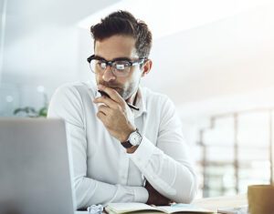 A shipping professional sits at his desk and looks at his laptop contemplating the information he’s viewing.