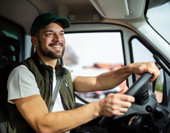 A truck driver behind the wheel of his truck, turning the wheel while smiling