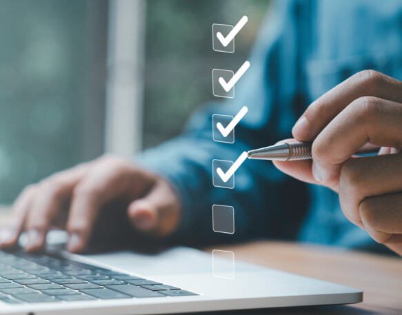 A person is using a laptop computer and holding a pen, checkmarks